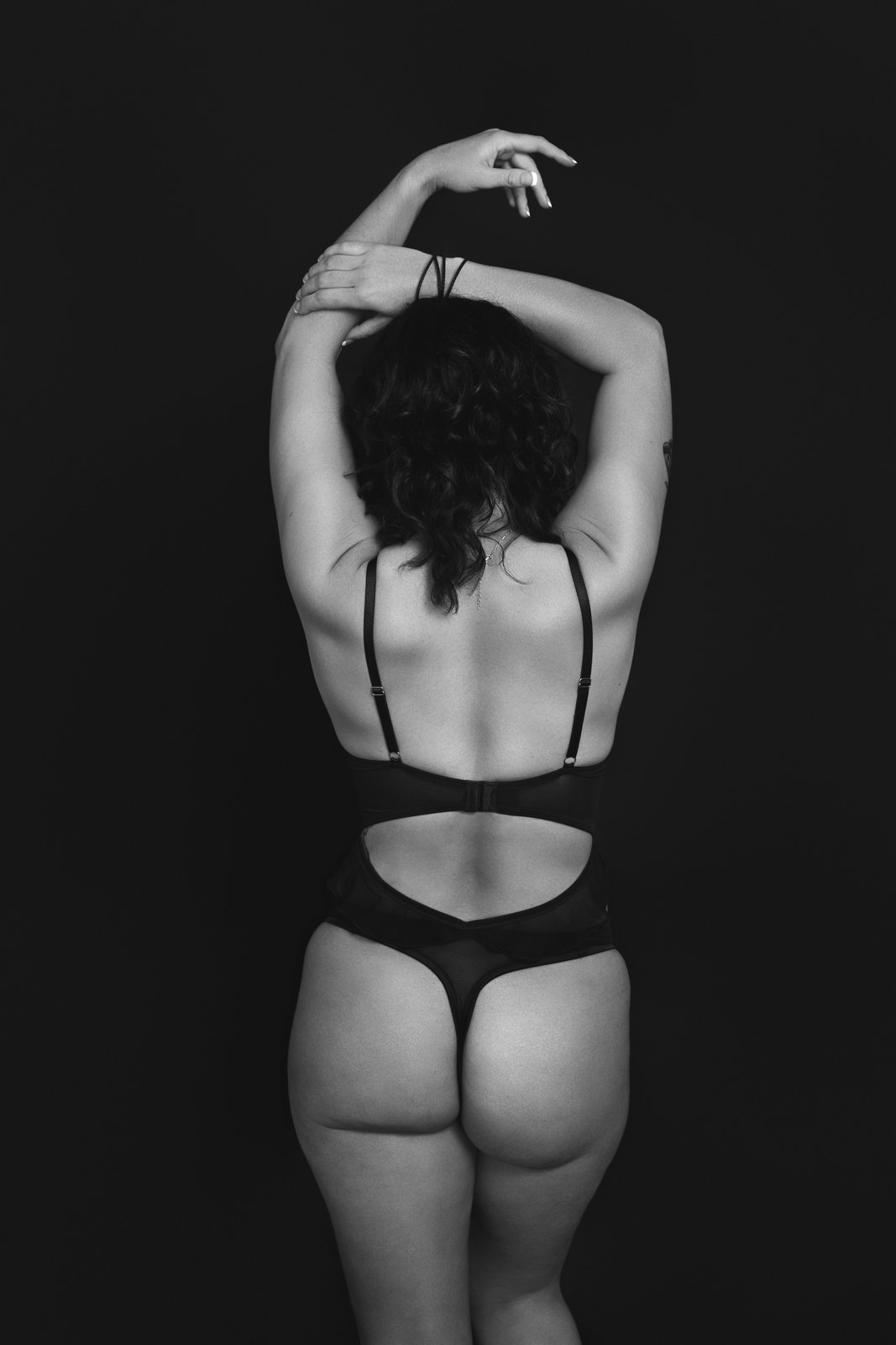 Black and white boudoir photograph from behind with arms raised