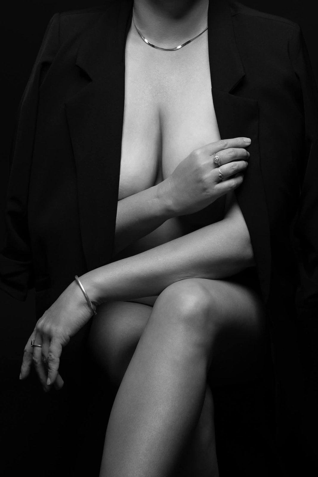 Black and white boudoir photograph of a woman seated in an open blazer